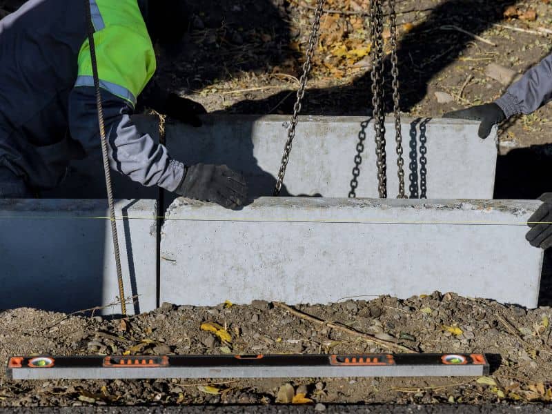 Workers installing concrete drainage structures using precise grade control during a road construction project